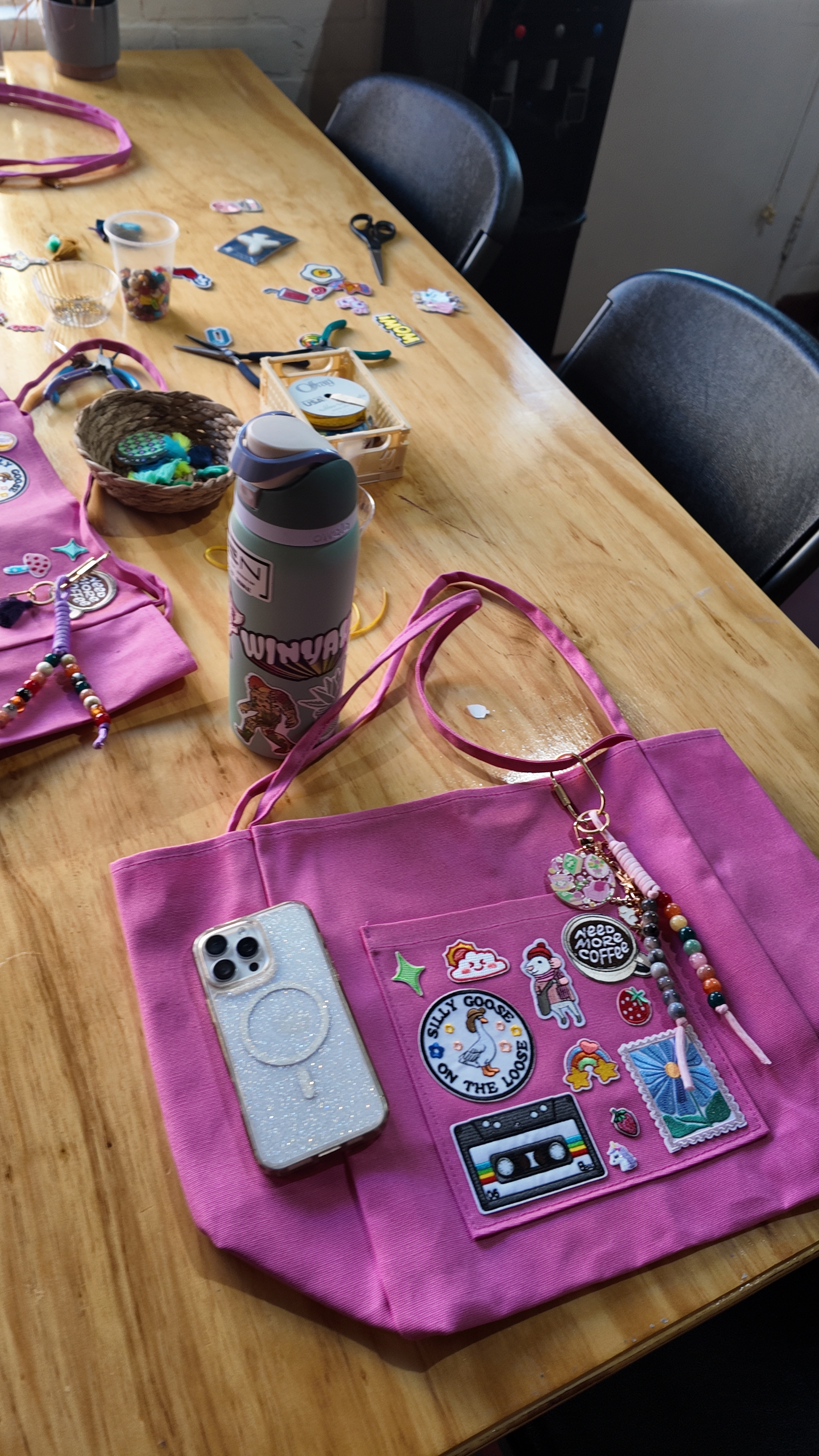 Pink tote bag with handmade charms and patches on a craft table